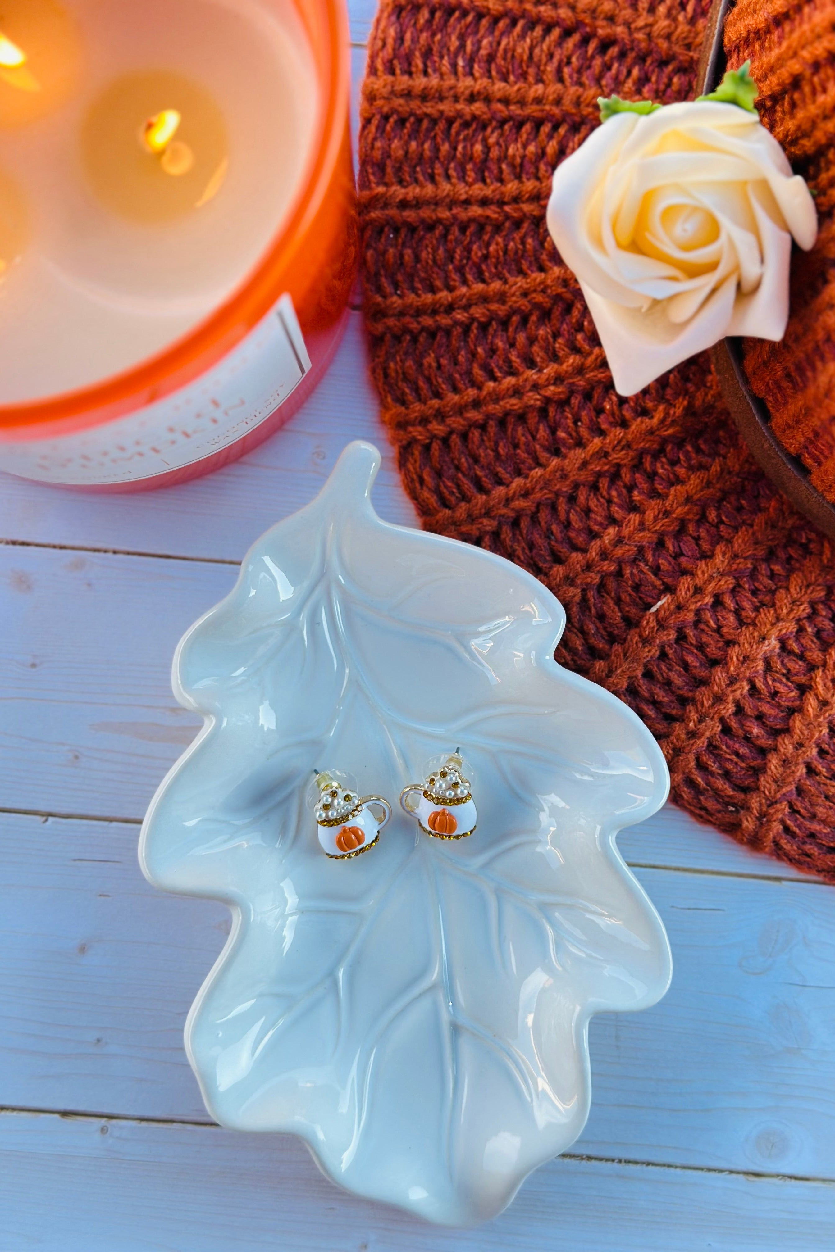 Pair of earrings on a leaf-shaped dish with a candle and knitted item in the background.