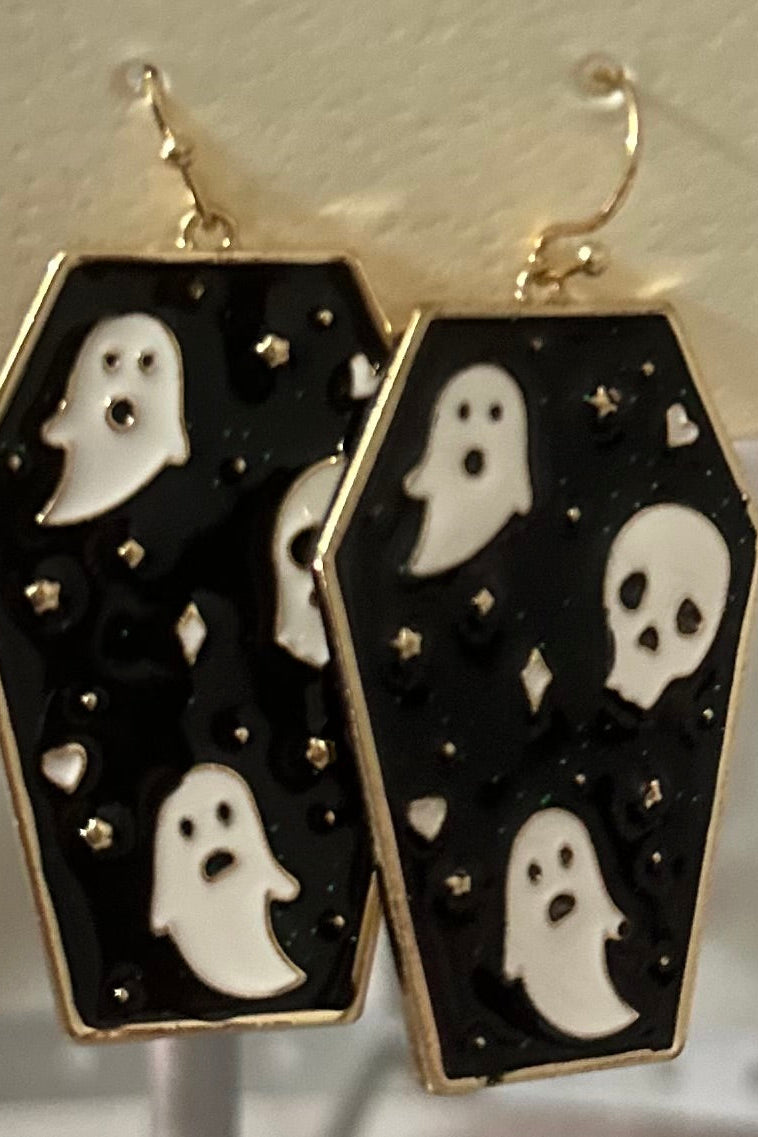 A pair of black and gold colored earrings featuring a pattern of white ghosts with black backdrops and gold accents displayed on a mannequin jewelry stand.