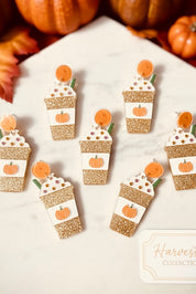 Pumpkin spice latte earrings on a white surface with pumpkins and leaves in the background.
