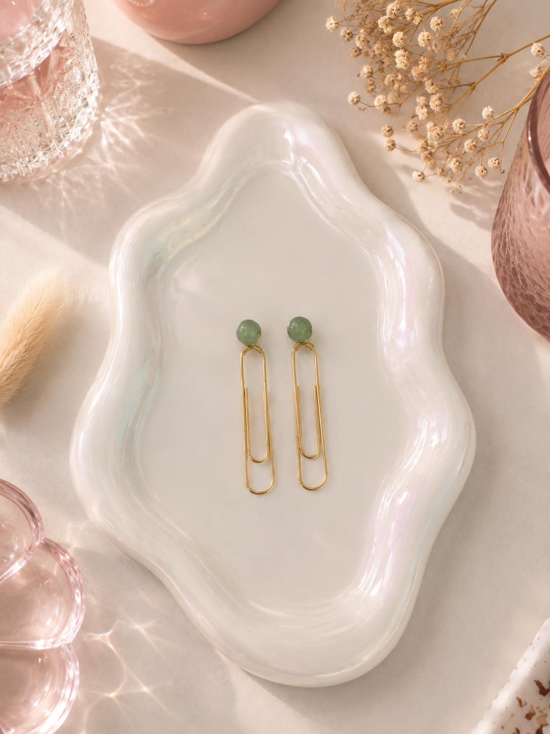 Two gold hair clips with green beads on a white dish with decorative items.