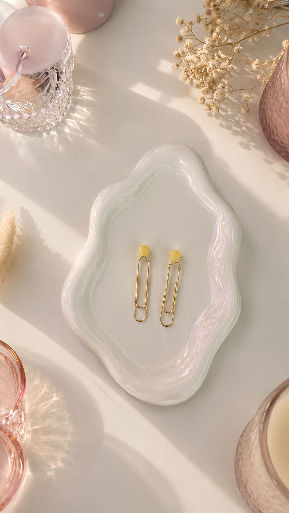 White jewelry dish with gold hair clips on a light pink surface with decorative elements.