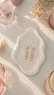 White jewelry dish with gold hair clips on a light pink surface with decorative elements.