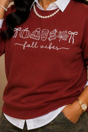 A woman wearing a burgundy crewneck sweatshirt with white text reading 'TOBACCO fall winter' over a white collared shirt, shown in a two-panel lifestyle photo with beige drapery and decorative books.