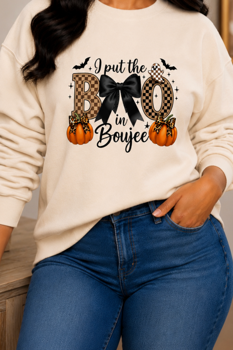 A woman wearing a cream-colored crewneck sweatshirt with a 'I just love Halloween' graphic featuring a cat, pumpkins, and bats, paired with blue jeans, in a cozy indoor setting.
