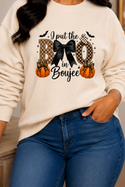 A woman wearing a cream-colored crewneck sweatshirt with a 'I just love Halloween' graphic featuring a cat, pumpkins, and bats, paired with blue jeans, in a cozy indoor setting.