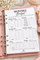 A monthly budget planner insert page displayed in a pink ring binder, with decorative flowers and a gold-toned accessory in the background.