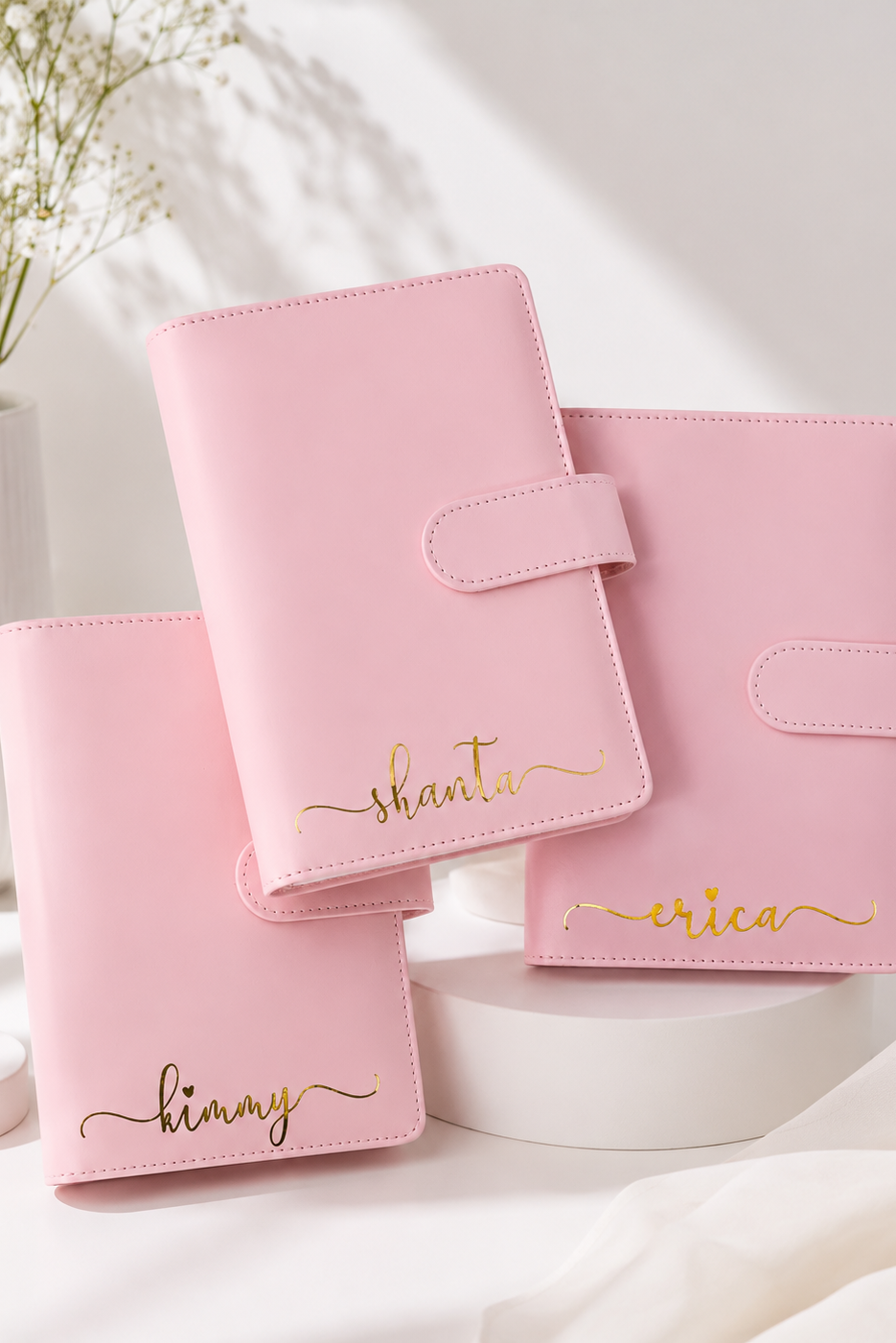 Set of pink personalized planners on a white surface with a vase in the background
