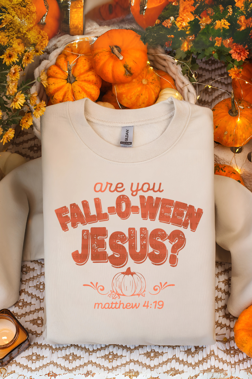 White sweatshirt with 'are you Fall-o-ween Jesus?' text in an autumn-themed setting with pumpkins and foliage.