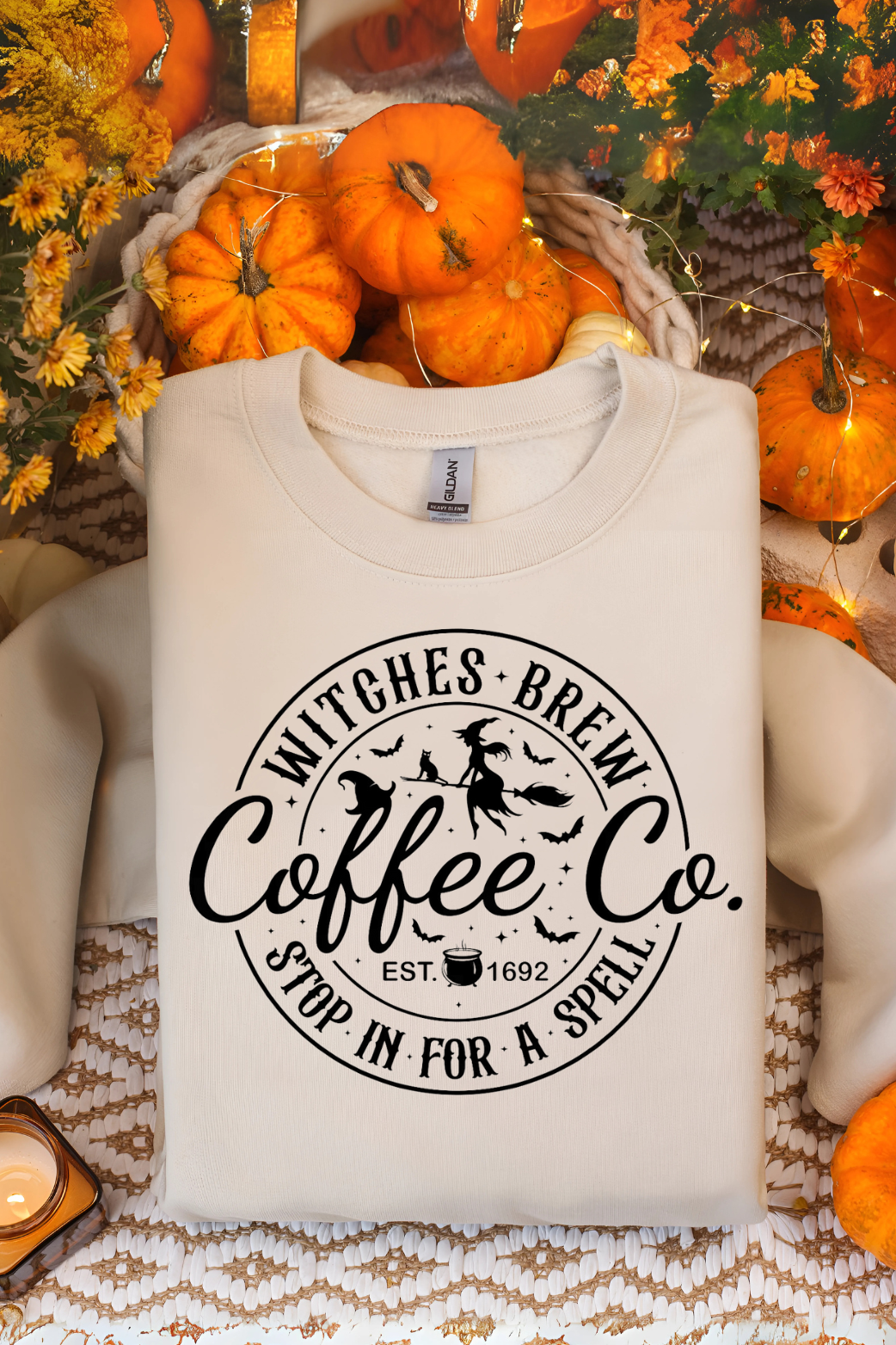 White sweatshirt with 'Witches Brew Coffee Co' print on a festive background with pumpkins and flowers.