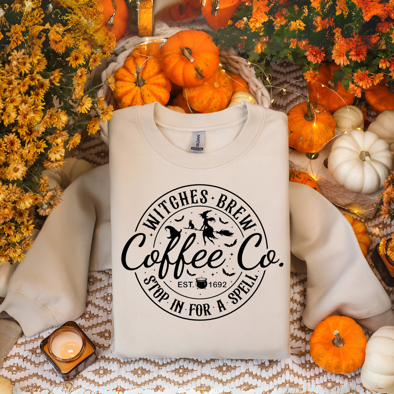 White sweatshirt with 'Witches Brew Coffee Co' print on a festive background with pumpkins and flowers.