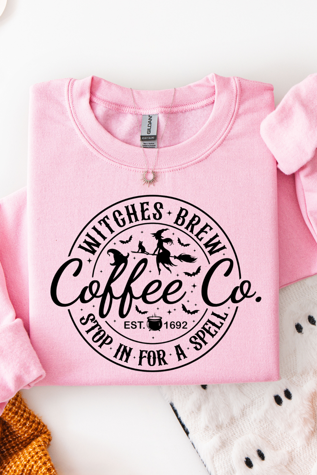 Pink sweatshirt with 'Witches Brew Coffee Co.' text on a Halloween-themed background