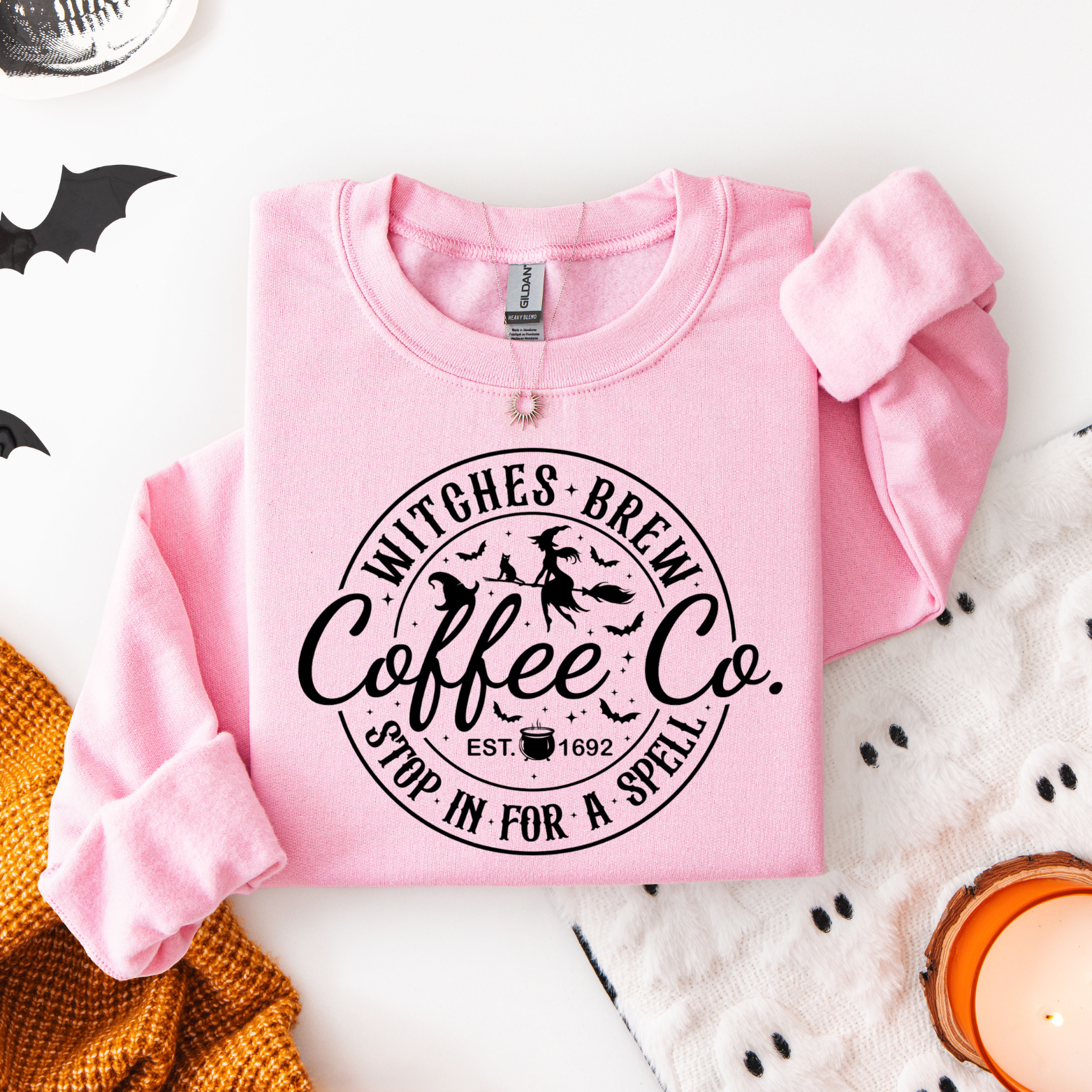 Pink sweatshirt with 'Witches Brew Coffee Co.' text on a Halloween-themed background