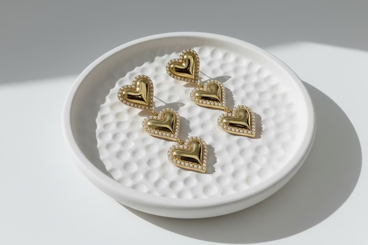 Gold heart-shaped earrings on a textured white dish